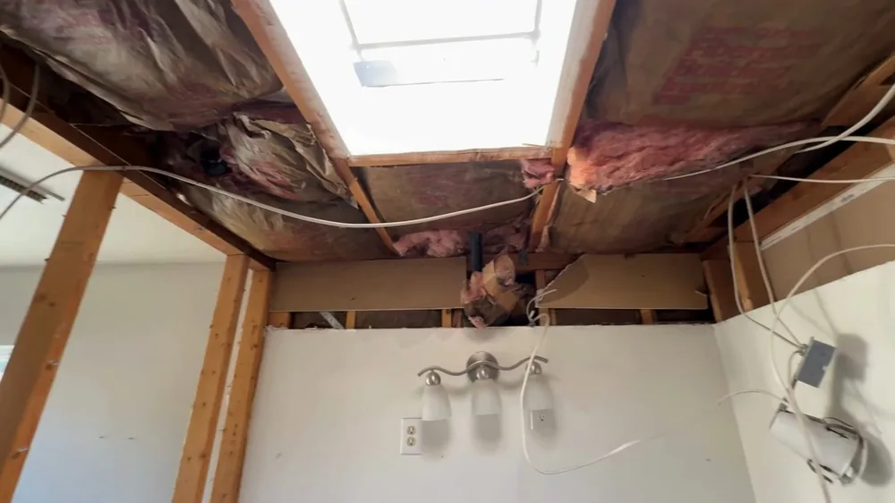 Bathroom ceiling opened to the joists with insulation and a skylight above a vanity light