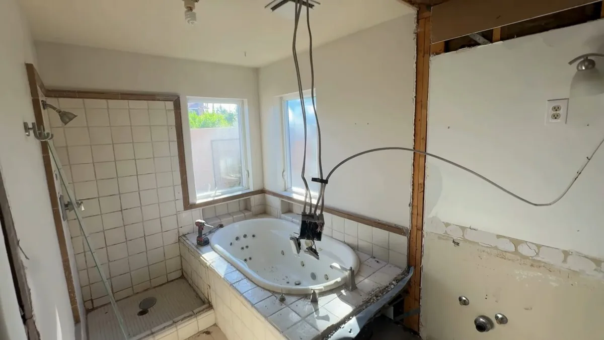 Bathroom with a tub, tile and wall sections removed and wires hanging from the ceiling