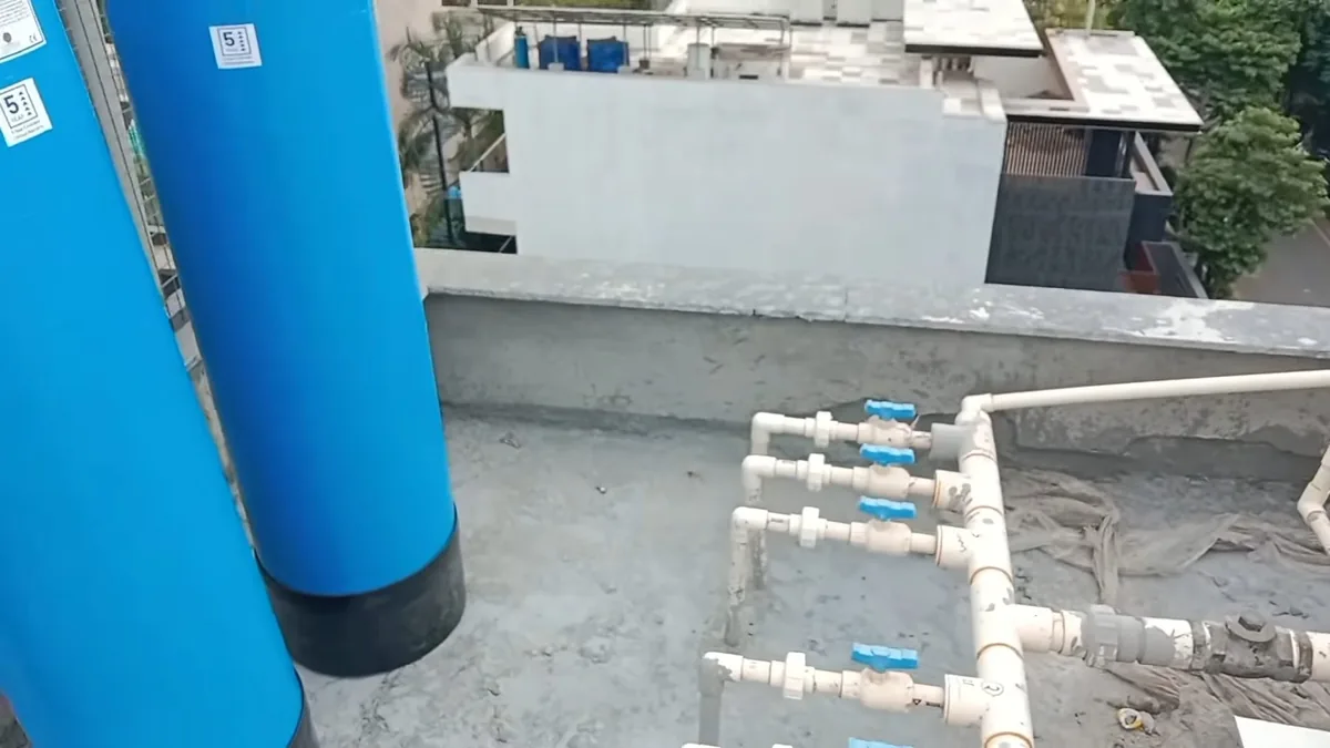 Two tall blue softener tanks beside a manifold of white pipes with blue valves