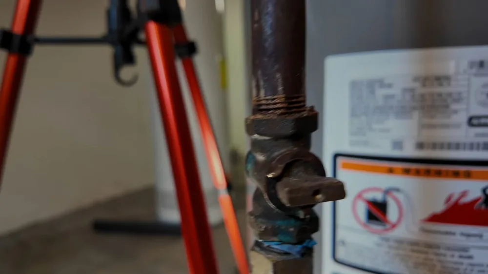 Brass shutoff valve on a supply pipe beside a gas water heater with warning labels