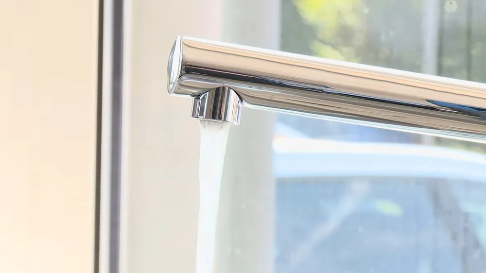 Chrome faucet running water in a bright kitchen window