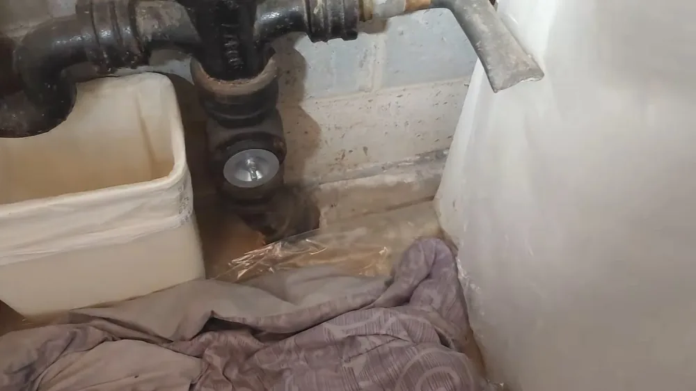 Black cast iron drain fittings at a bathroom floor opening beside a cinder block wall