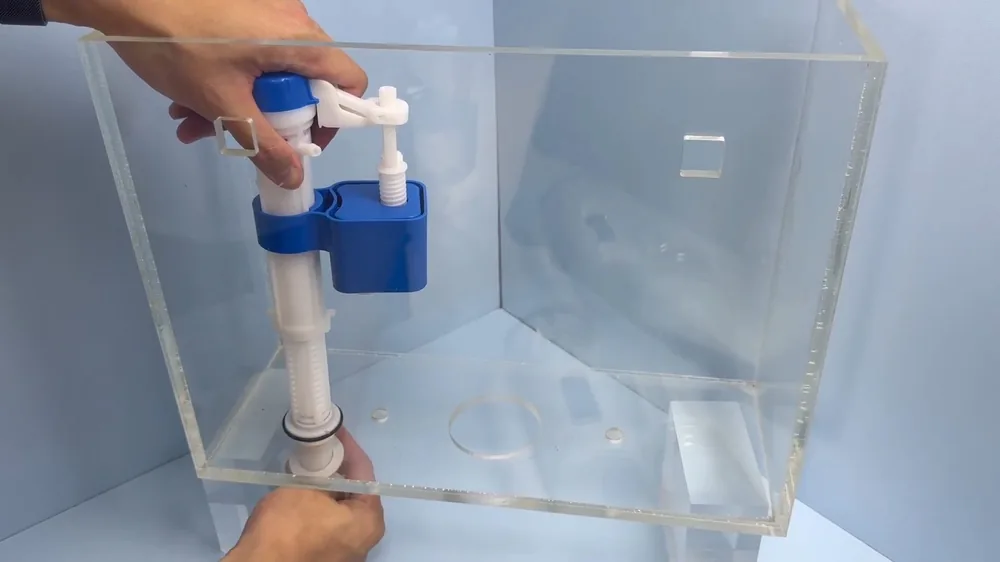 Hands holding a blue and white fill valve inside a clear acrylic toilet tank model