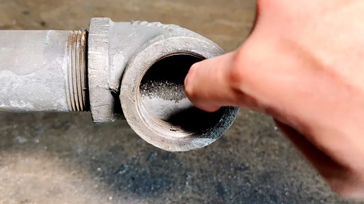 Finger pointing into an open cast-iron cleanout fitting