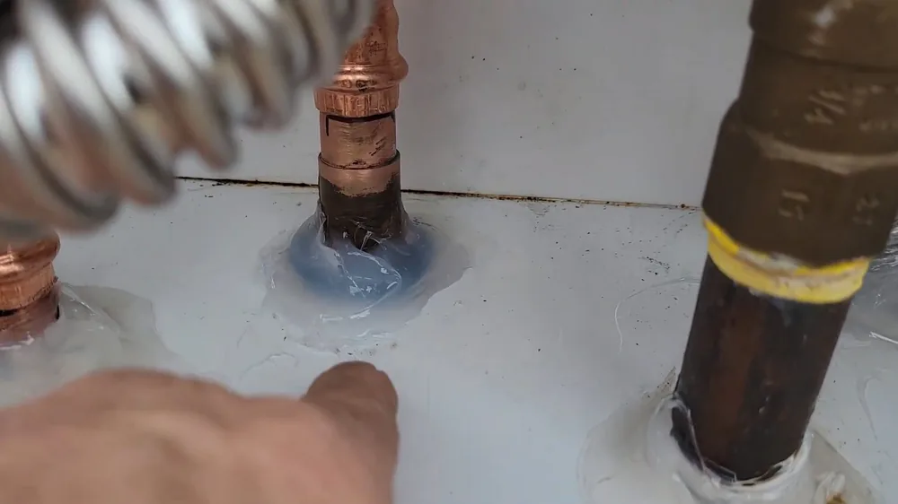 Hand beside a flexible gas line, a copper water pipe and a black iron gas pipe entering the top of a white heater
