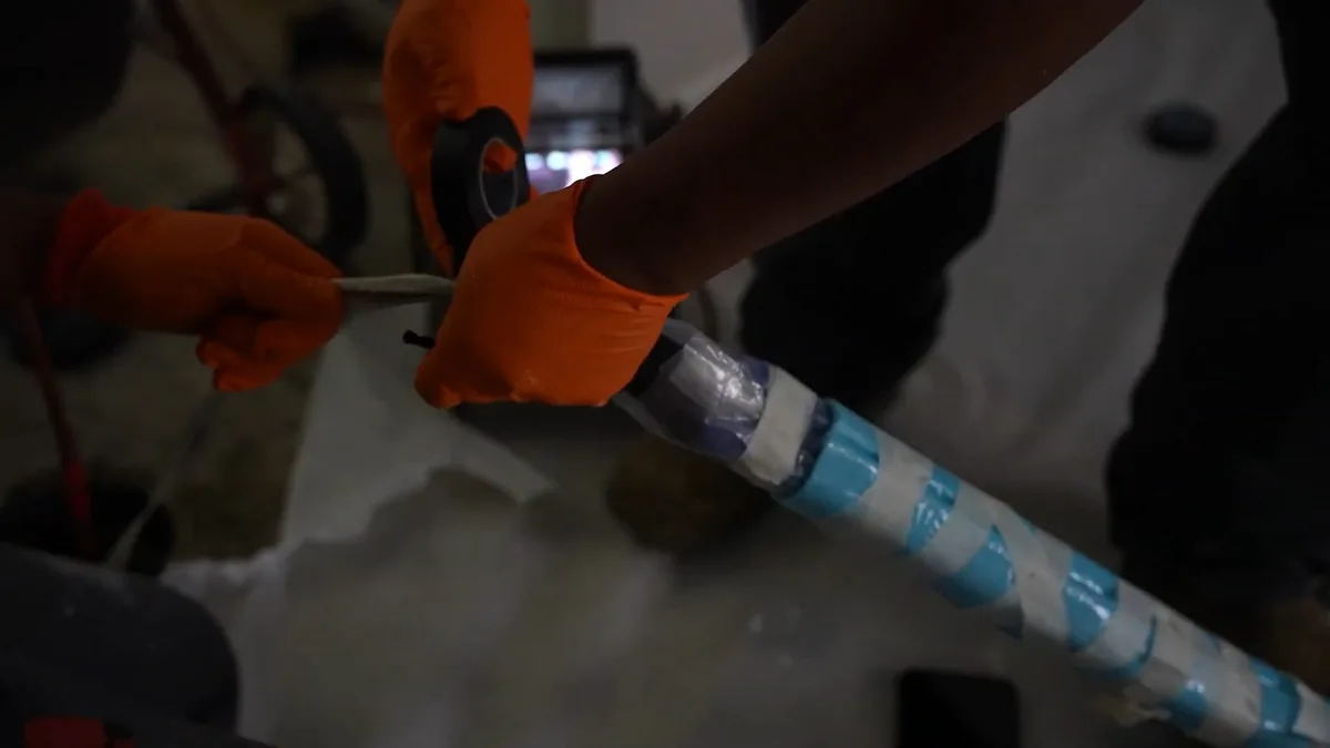 Orange-gloved hands feeding a blue-striped lining tube