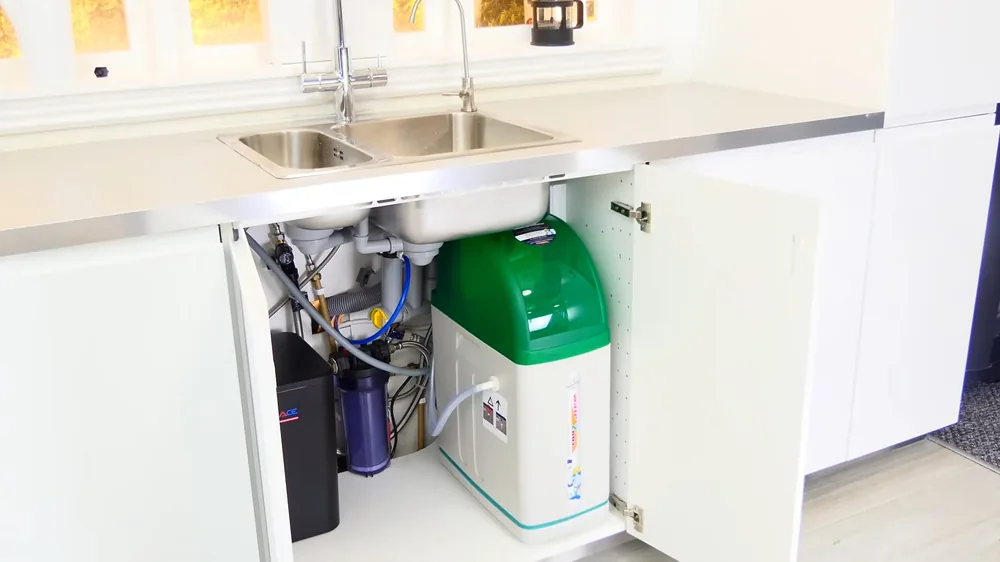 Green water softener standing in an open cabinet under a double kitchen sink