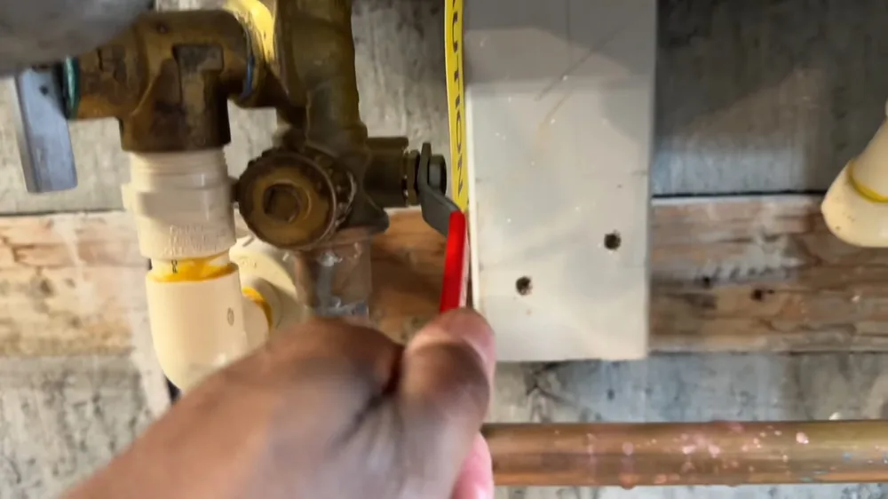 Hand holding a tape measure beside brass service valves under a tankless heater