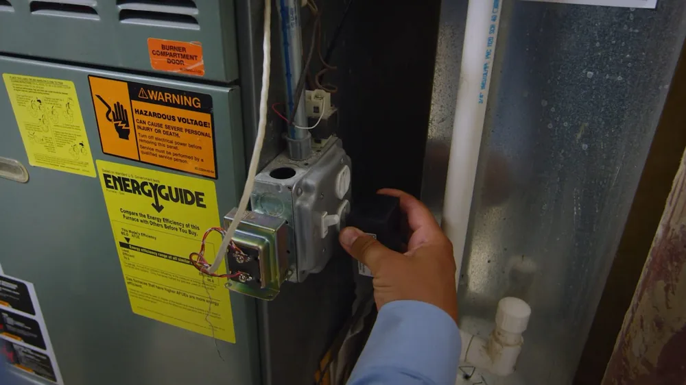 Hand resting on the gas control panel of a water heater under a yellow energy label