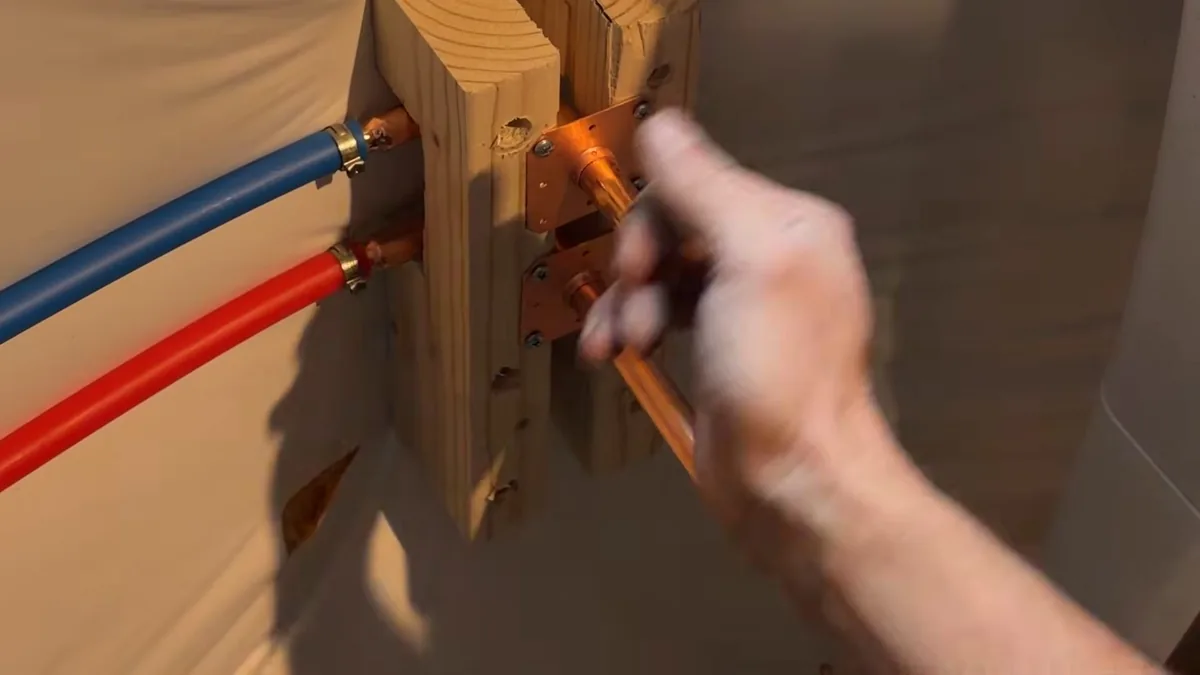 Hand adjusting copper stub-outs on a wooden bracket with red and blue flexible supply lines attached