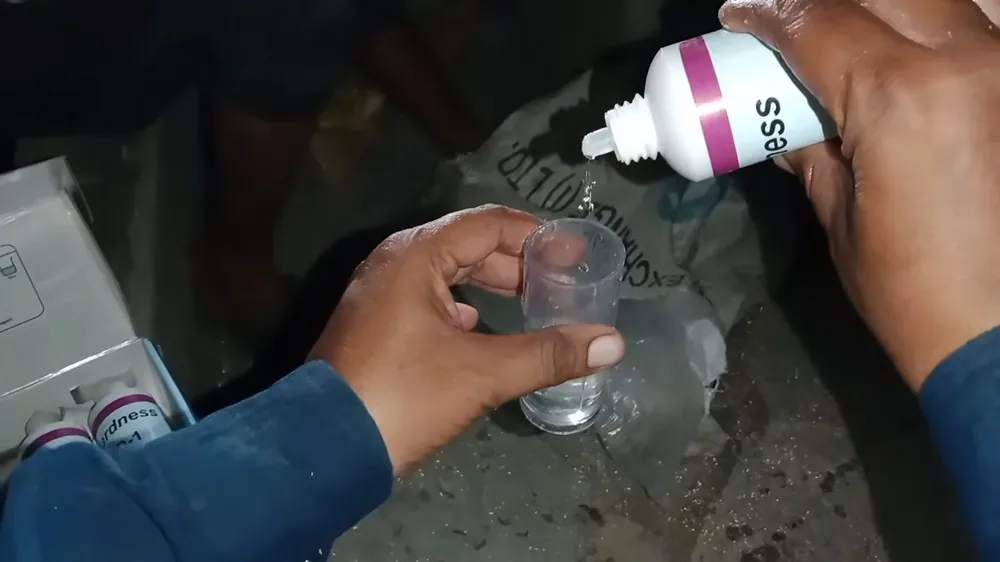 Hands holding a small clear cup while drops from a test bottle fall into the water