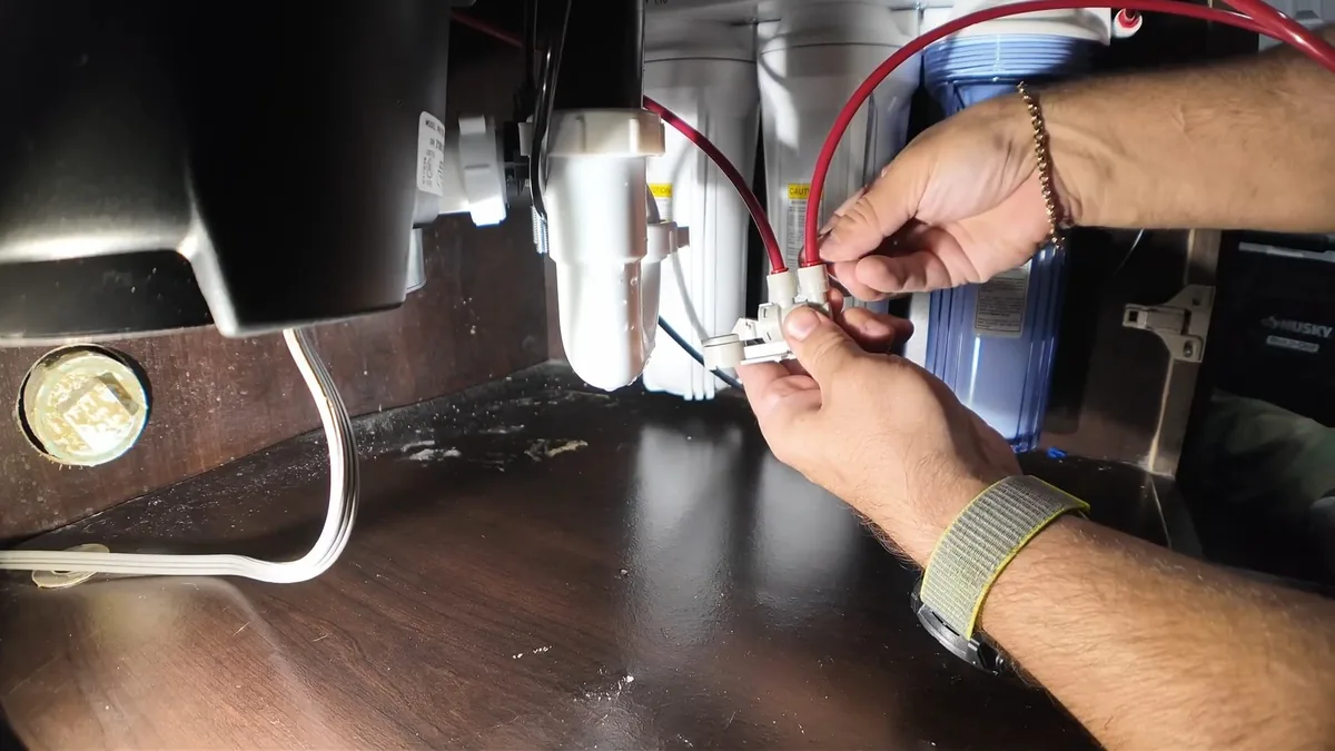 Hands connecting small wires beneath a sink above water filter housings