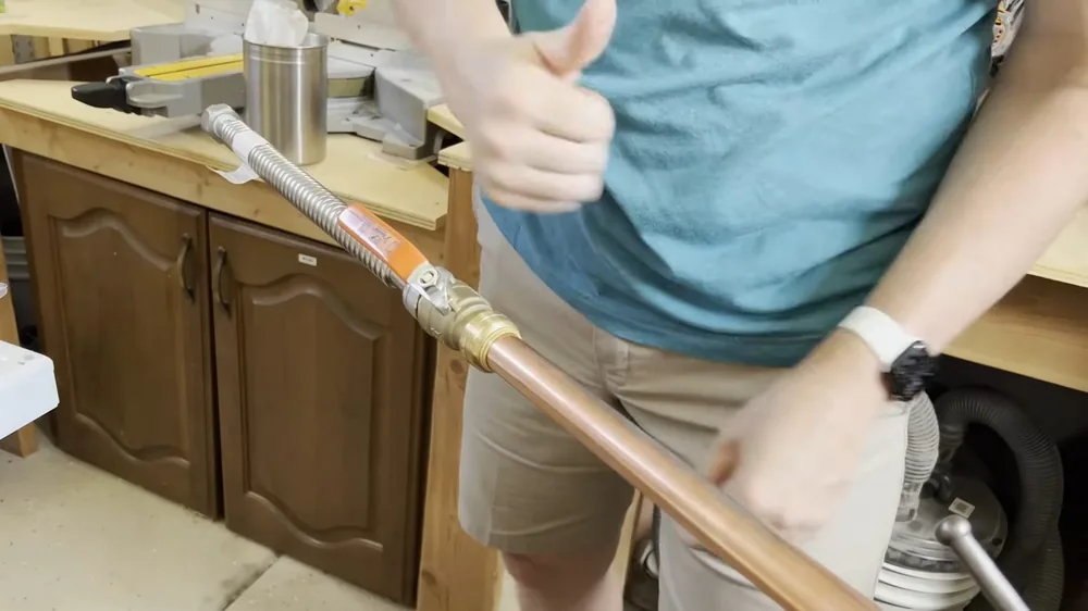 Hands holding a flexible copper connector beside wooden cabinets