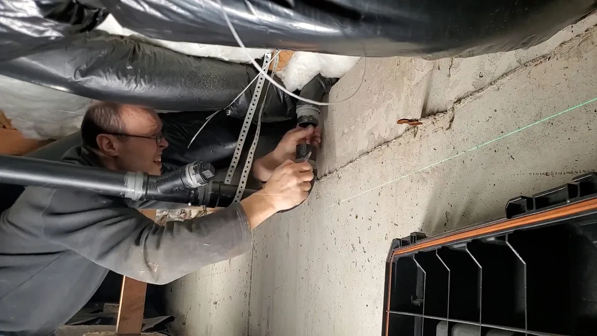 Man reaching along a pipe run in a tight space beneath a floor with a laser line across the wall