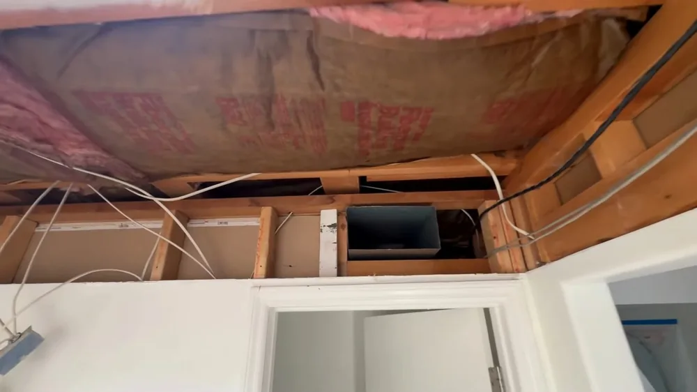 Ceiling opened between joists above a doorway, showing pink insulation and loose wiring