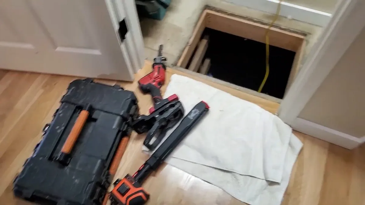 Plumbing tool case, wrenches and a towel laid out beside an open floor access hatch