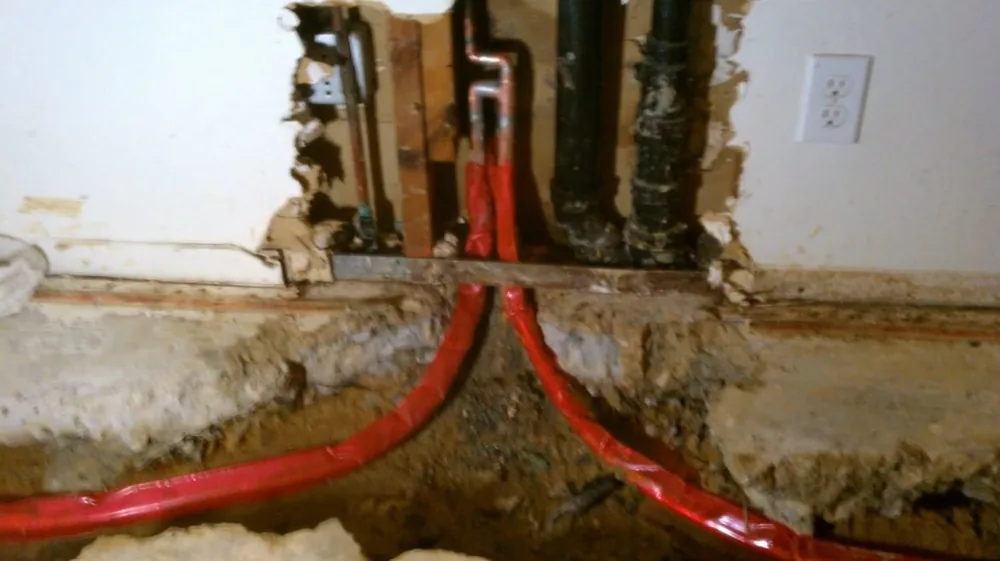 Two red flexible supply lines running down through an opened wall near an outlet