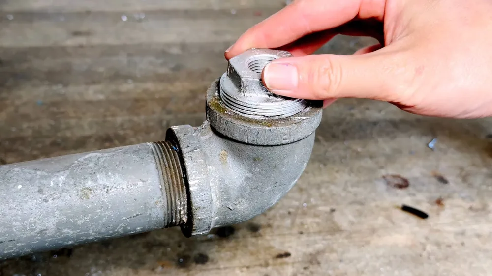 Hand unscrewing the cap from a galvanized cleanout elbow