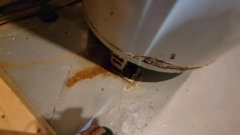Orange rust stain on a cracked floor beneath the rim at the base of a tank water heater