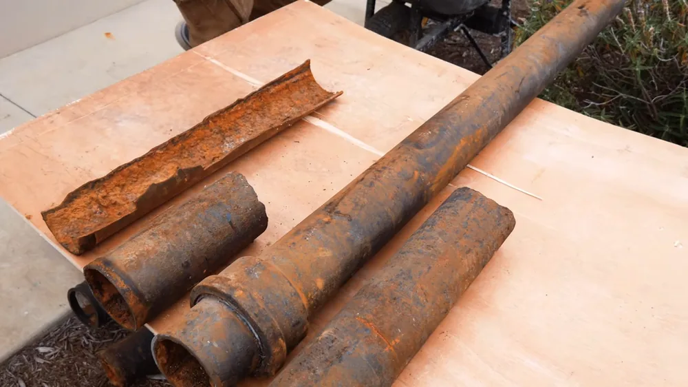 Several cut lengths of rust-covered cast iron pipe lying on a sheet of plywood outdoors