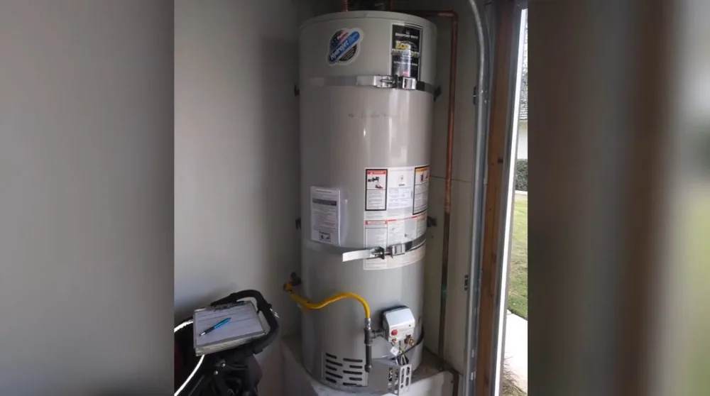 Gas tank water heater standing in a narrow utility closet with a yellow gas line and a small device at its base