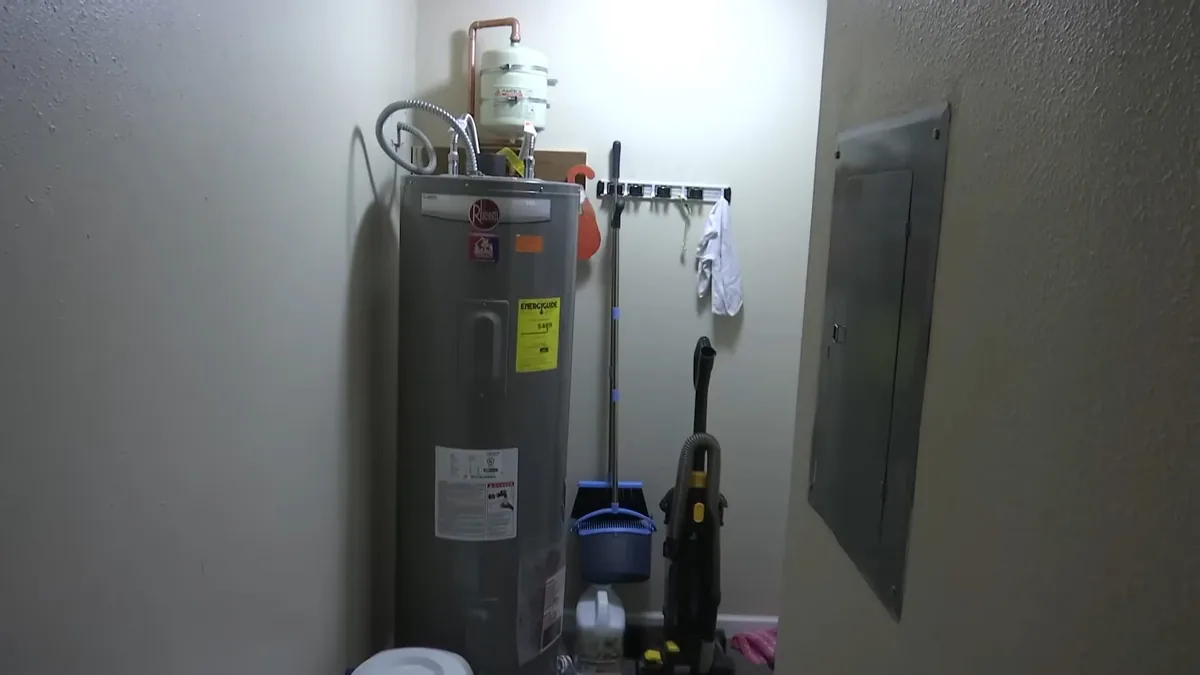 Gray tank water heater standing in a utility room beside an electrical panel