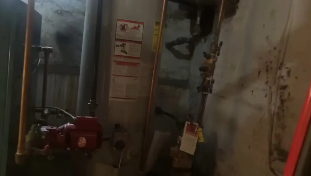 Dim utility room with a tank heater, copper supply pipes and valves along a concrete wall