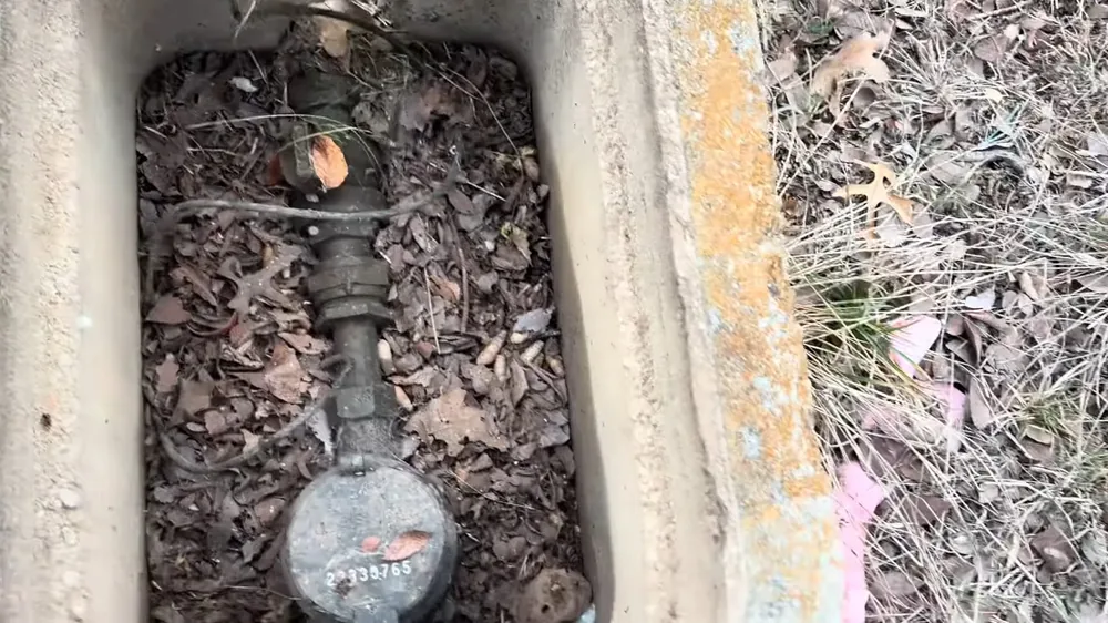 Water meter and valve in a concrete ground box partly covered with dry leaves